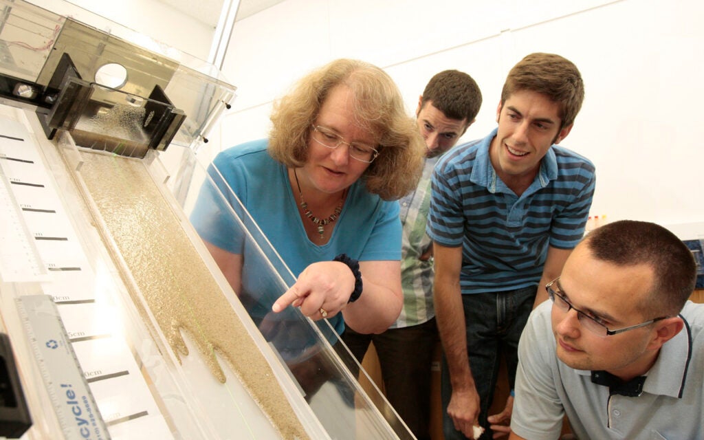 Photo of a class studying the flow of non-toxic liquids combined with glass beads to simulate the dynamics of the movement of oil that has saturated beach sand.