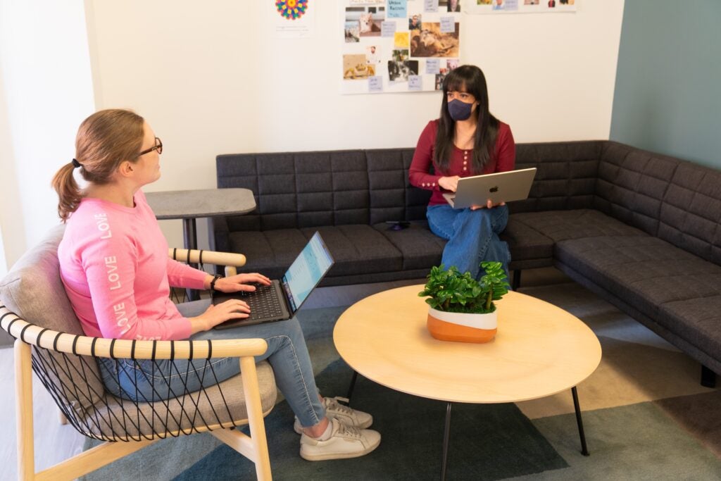 Two TLC staff members talking seated on a couch with laptops
