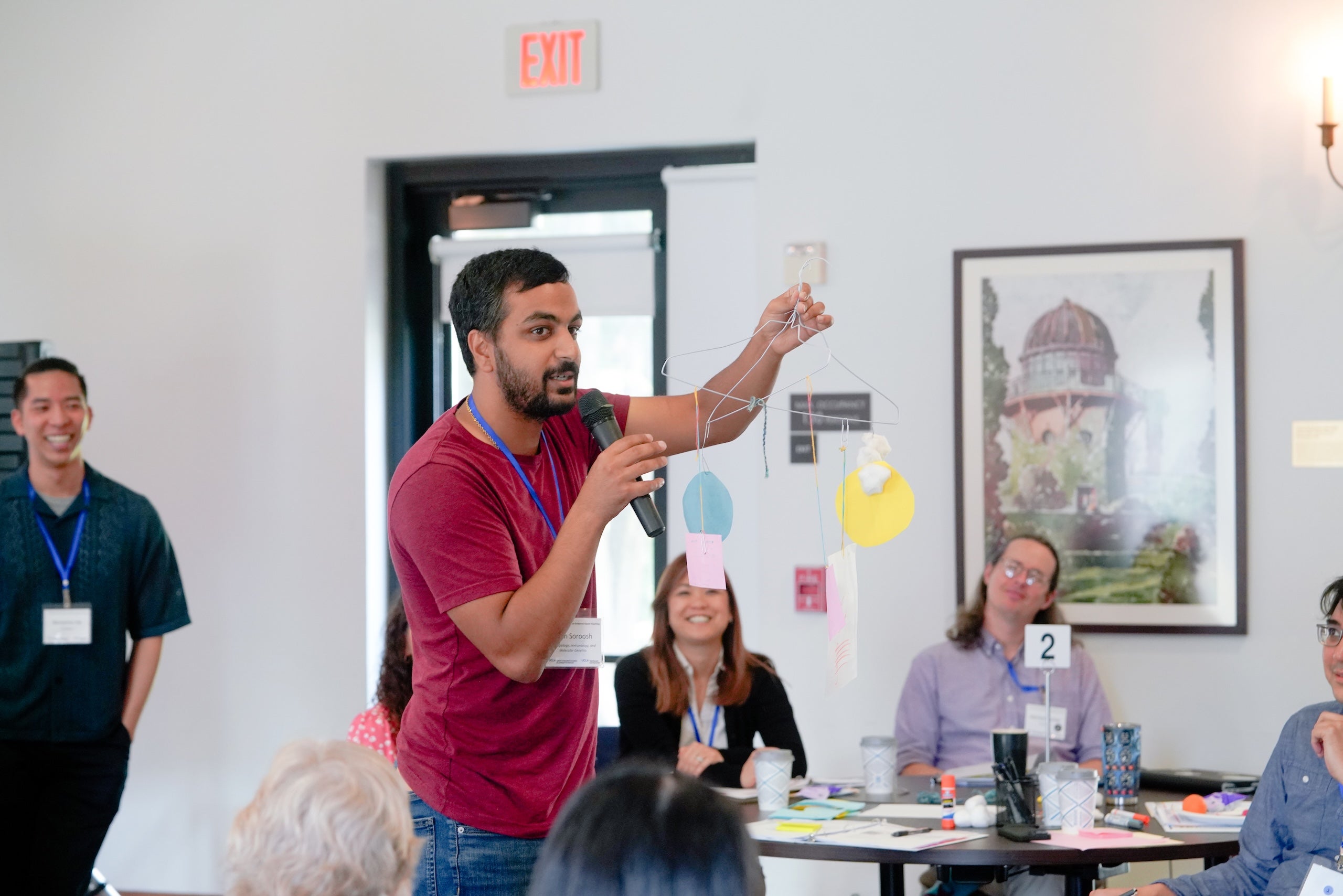 An instructor holds a mobile made of paper and wire while speaking into a microphone