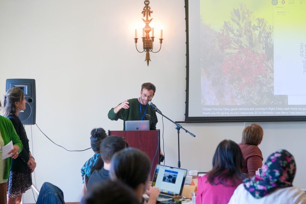 An instructor stands at a podium with a powerpoint behind them.