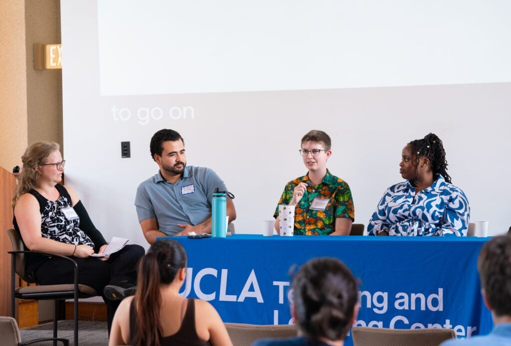 Four conversation panelists seated at a raised table with a blue tablecloth in a lecture hall.
