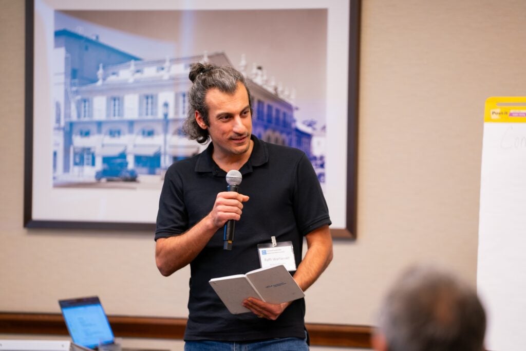 Raffi Wartanian stands and speaks into a microphone holding a notebook