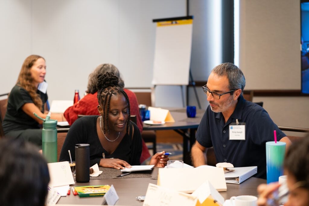 Two participants sit at a table and speak to each other while reviewing a notebook