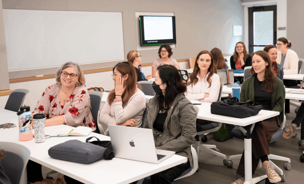 Vice Provost Erin Sanders O'Leary seated at a lecture hall table talking with TLC staff