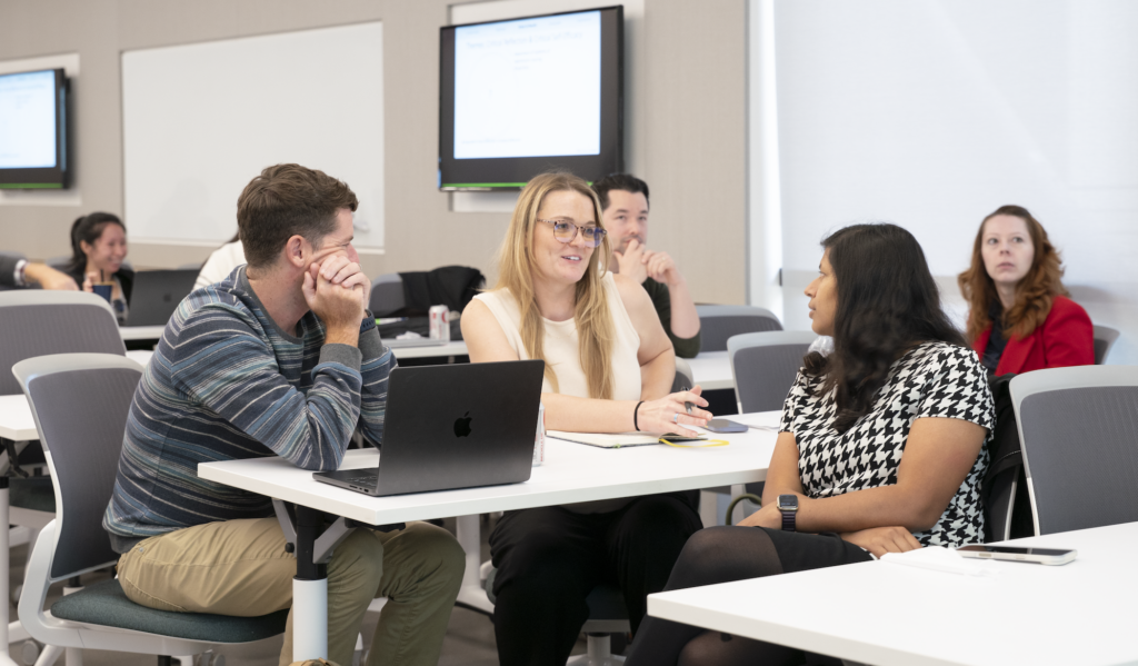 Instructors in conversation seated at lecture desks with laptops