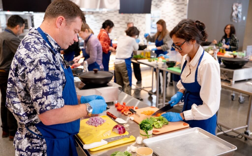 Participants prep ingredients at work stations in the Tipuana Teaching Kitchen