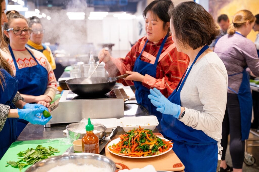 Participants gather around a stove and cook ingredients