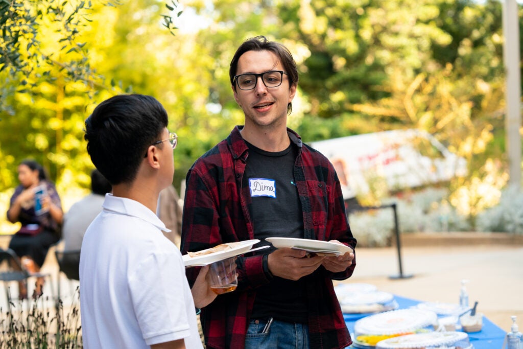 Dima Vaido stands in the botanical garden in conversation with another awardee.