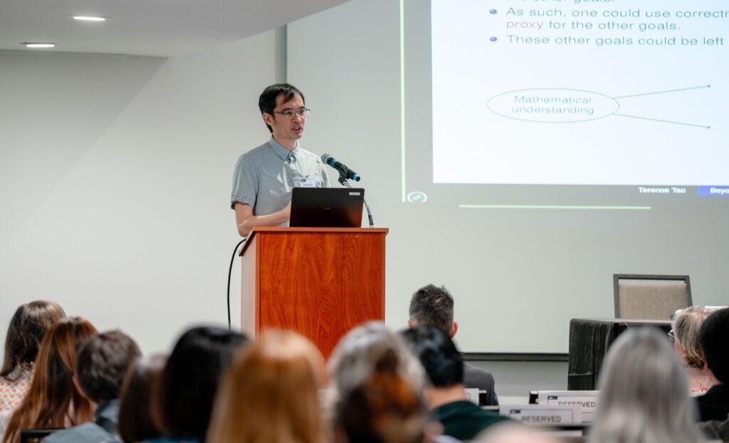 Professor Terence Tao speaks at a podium to a crowd during the keynote address.