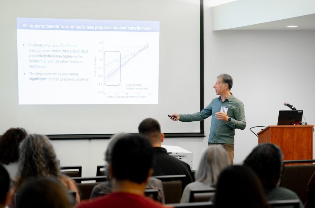 A professor stands before an audience and lectures with a PowerPoint presentation.