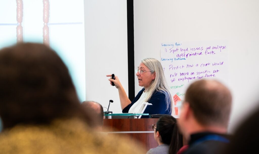 Deb Pires speaks to Summer institute attendees in a large classroom.