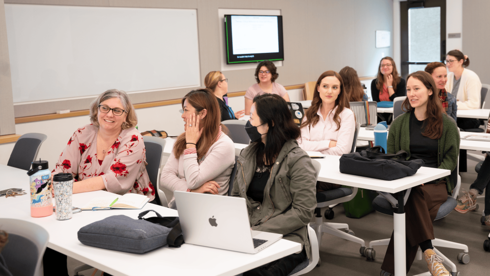 Vice Provost Erin Sanders O'Leary seated at a lecture hall table talking with TLC staff