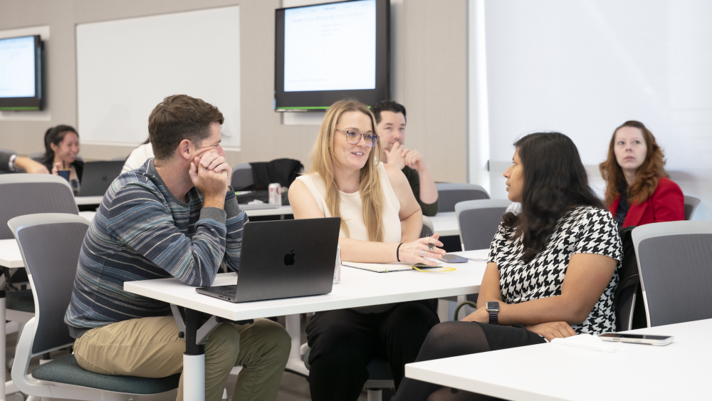 Instructors in conversation seated at lecture desks with laptops