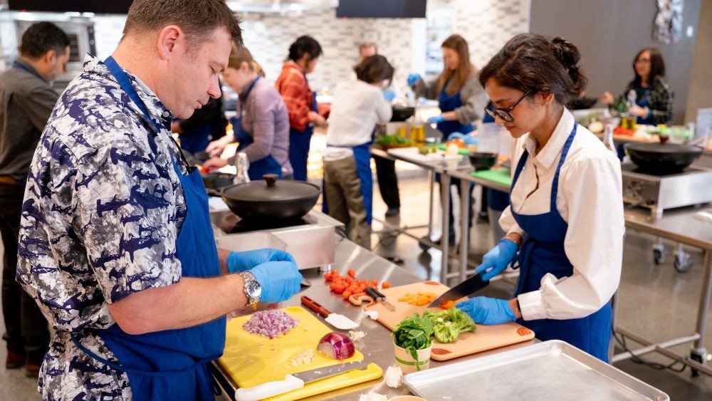 Participants prep ingredients at work stations in the Tipuana Teaching Kitchen