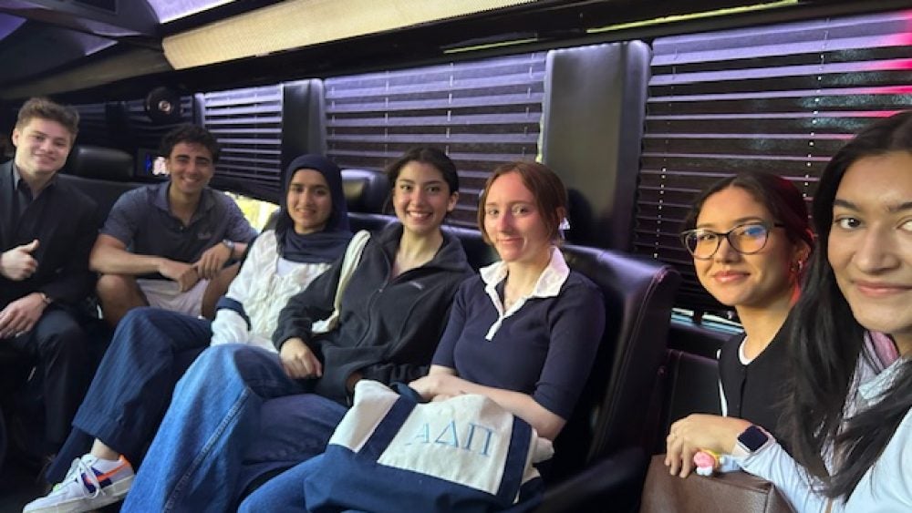Students seated in the interior of a bus smiling at the camera
