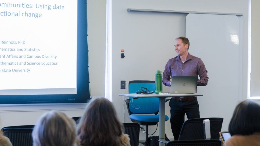 Image of a professor in front of a projector with text